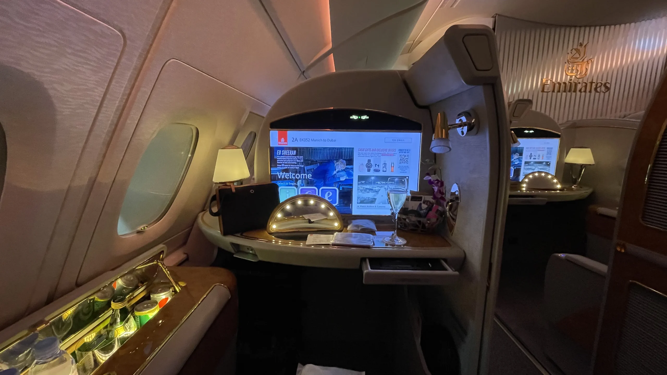 A wide view of the luxurious Emirates First Class suite, showing the lie-flat seat, personal minibar, and large entertainment screen.