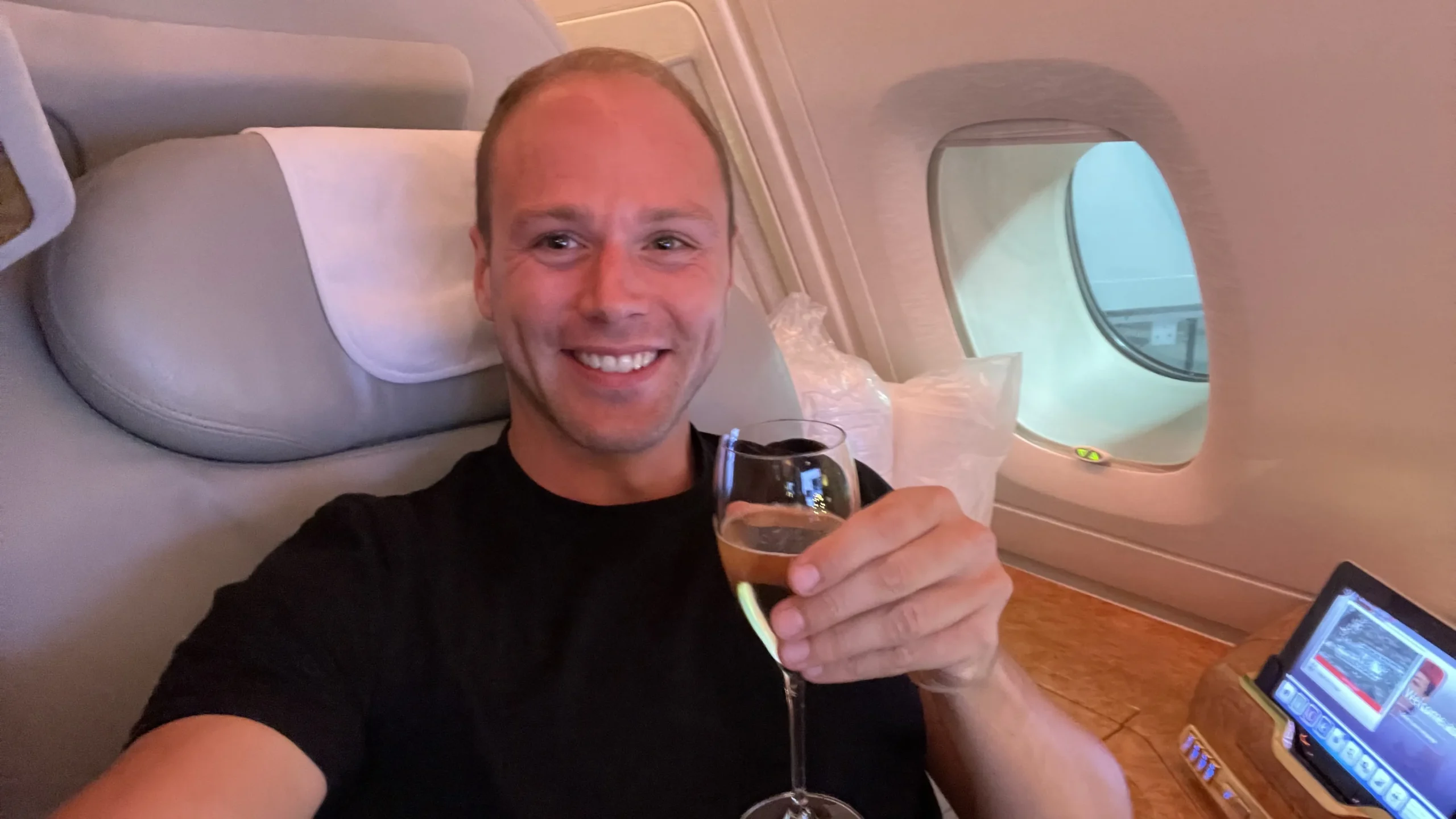 Smiling traveler relaxing in Emirates First Class seat with glass of champagne
