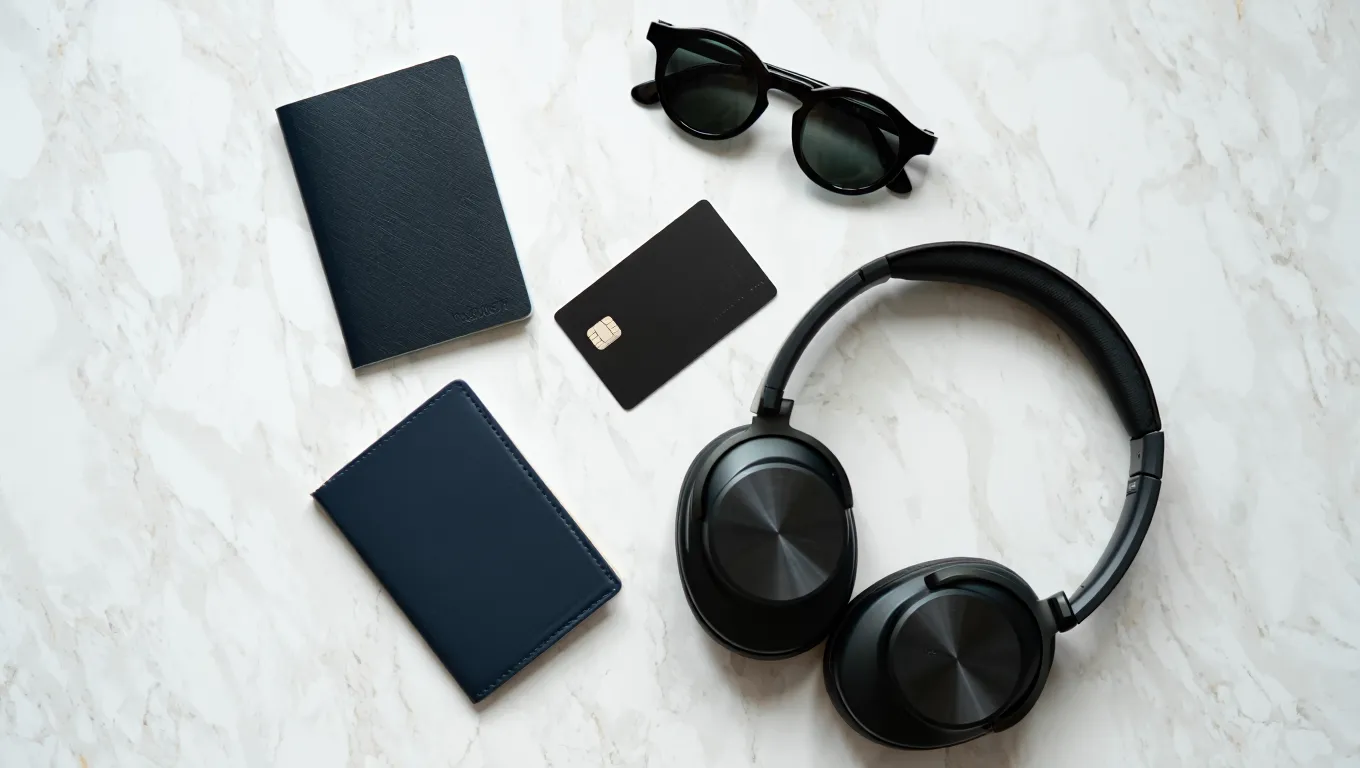 A flat lay of travel essentials including a passport, headphones, and a travel perks credit card.