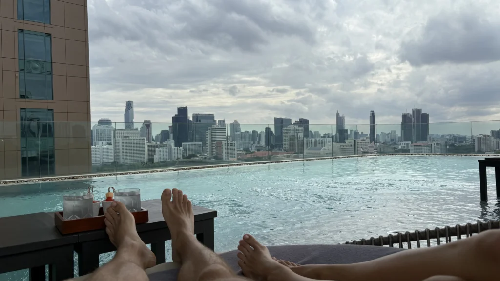 Relaxing by the rooftop infinity pool at Waldorf Astoria Bangkok with a panoramic view of the city skyline.