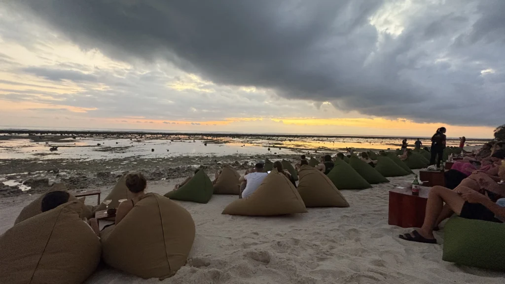 People relaxing on bean bags at Gili Trawangan beach during a colorful sunset with dramatic clouds over the ocean.
