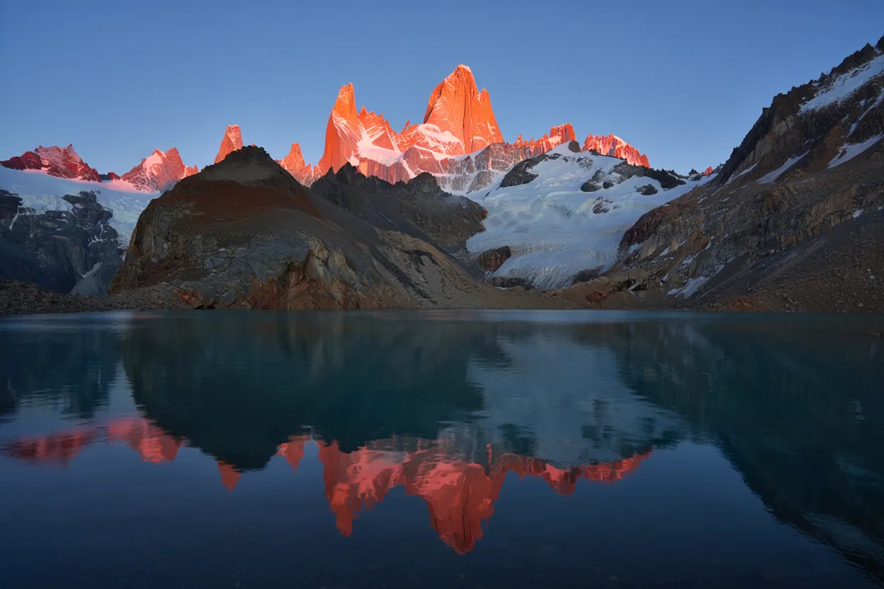 The iconic Mount Fitz Roy in Argentinian Patagonia, with its granite peaks glowing pink at sunrise and reflecting perfectly in the turquoise glacial lake below.