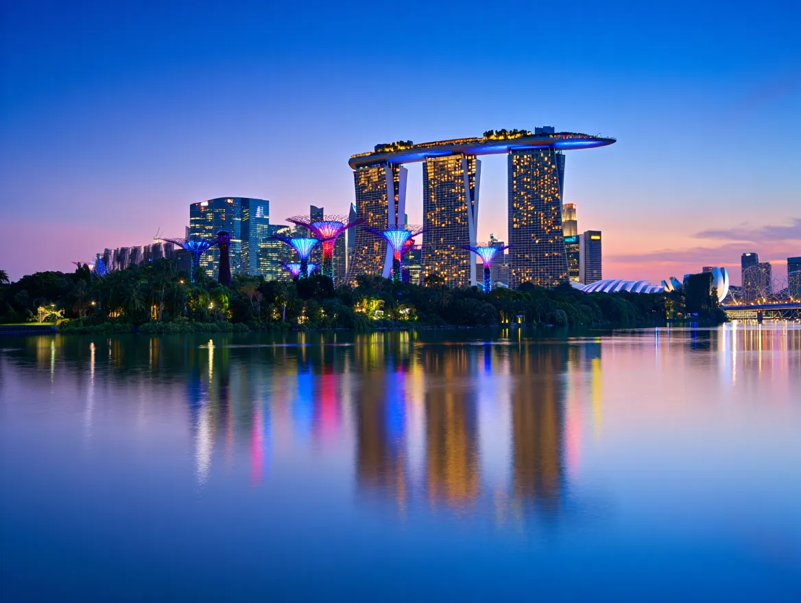 The futuristic Singapore skyline at blue hour, with the iconic Marina Bay Sands hotel and glowing Supertree Grove at Gardens by the Bay reflecting in the calm water.