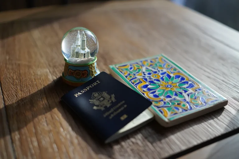A top-down photo of a passport on a wooden table. On one side of the passport is a snow globe containing a miniature European city, and on the other side is a colorful Mediterranean-style tile, symbolizing a single journey with two distinct destinations (Stopover Flight).