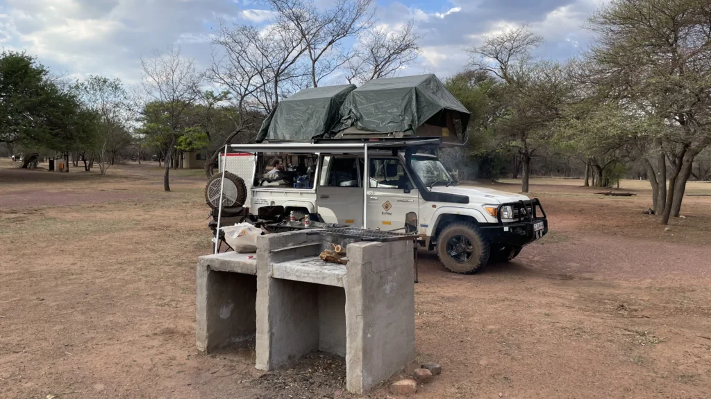 Off-road vehicle with rooftop tent parked at Bontle Campsite in Marakele National Park, next to a concrete braai area surrounded by dry trees and open bushveld.