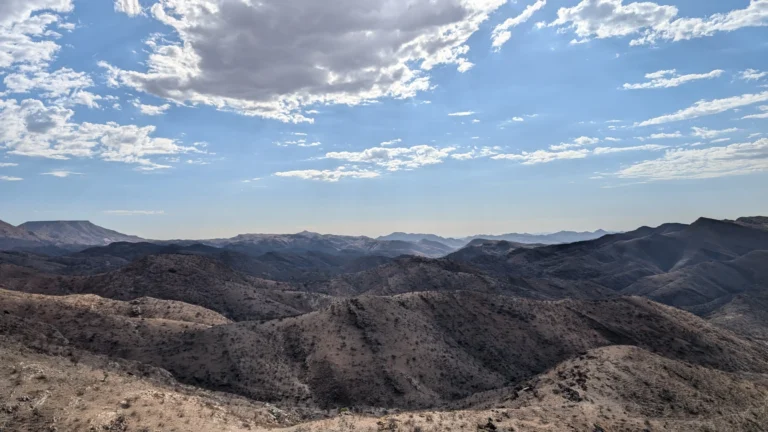 Hakos Astrofarm wide mountain landscape with rolling rocky hills under a bright blue sky scattered with clouds.