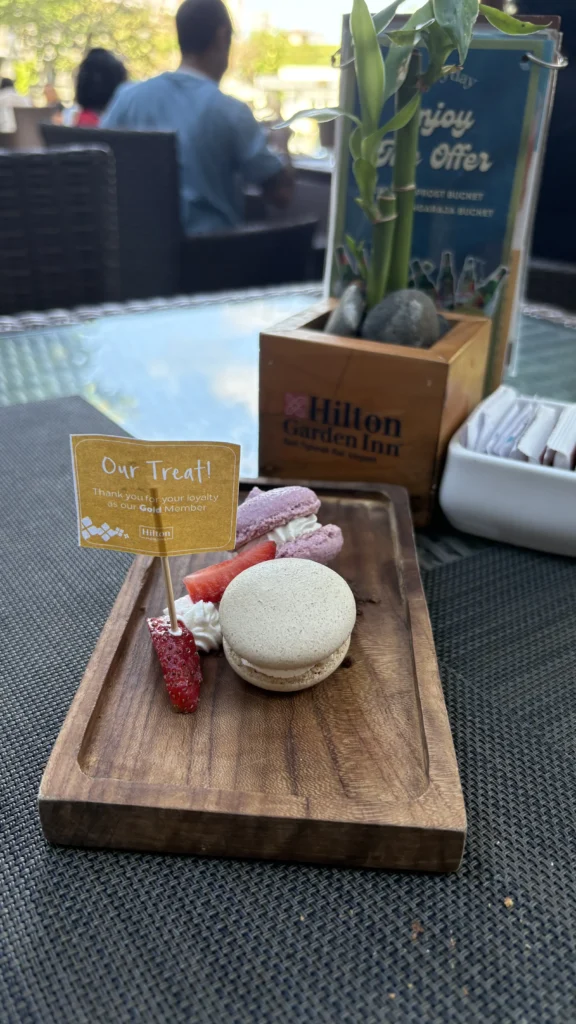 omplimentary dessert plate with a macaron, strawberries, and meringue served on a wooden tray at a Hilton Garden Inn, with a sign thanking a Gold member for their loyalty.
