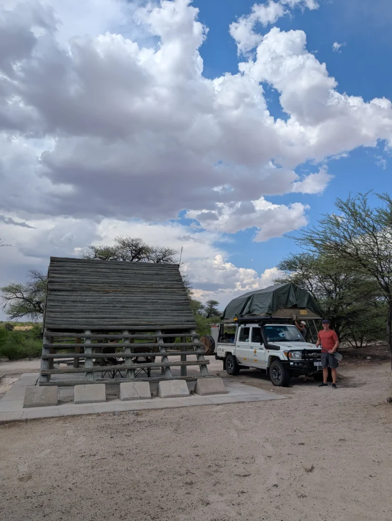 A 4x4 vehicle with a rooftop tent parked next to the iconic wooden A-frame shelter at Khiding Camp.