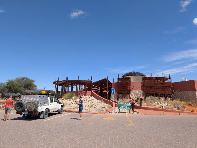 A white 4x4 vehicle parked in front of the main reception building at Twee Rivieren Rest Camp.