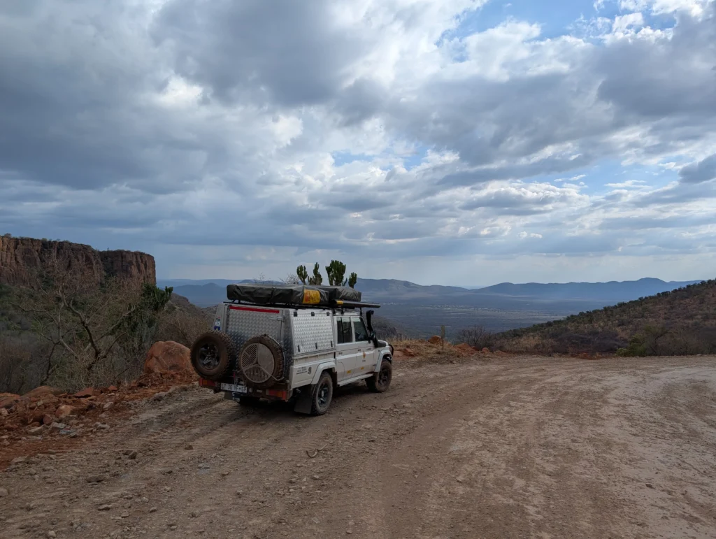 On our way to Bontle Campsite, off-road vehicle parked on a dirt mountain road overlooking a wide valley and dramatic cloudy sky in a remote, rocky landscape.