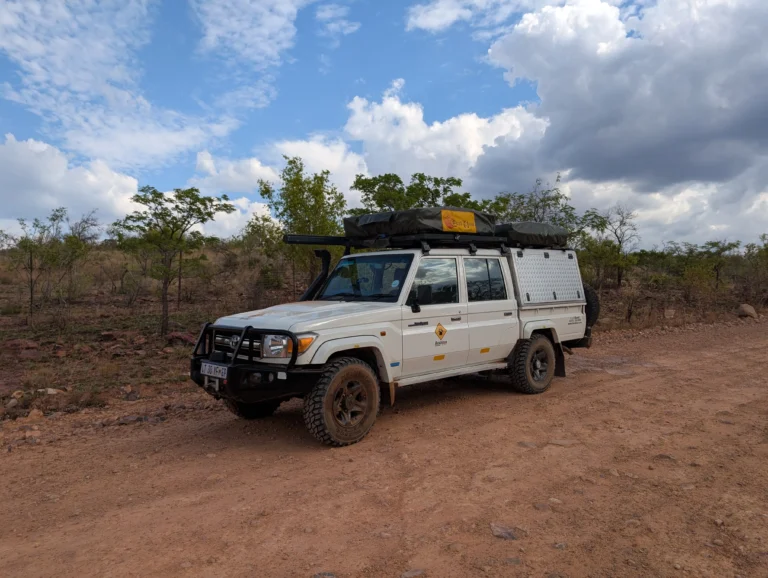 Bushlore Land Cruiser with rooftop tent driving on a dirt road starting our Safari with the first stop in Bontle Campsite surrounded by dry bush and a partly cloudy blue sky.