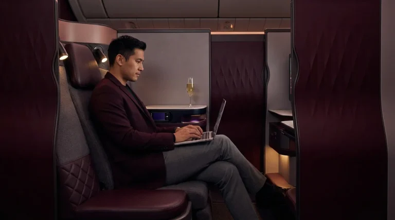 Qatar Airways Qsuite Business Class cabin interior showing private sliding door, burgundy seat details, and champagne on the console.